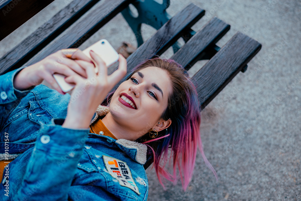 一个紫色头发的微笑女孩躺在长椅上打电话。