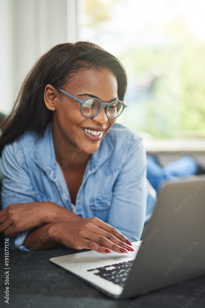微笑的非洲女人在沙发上用笔记本电脑放松