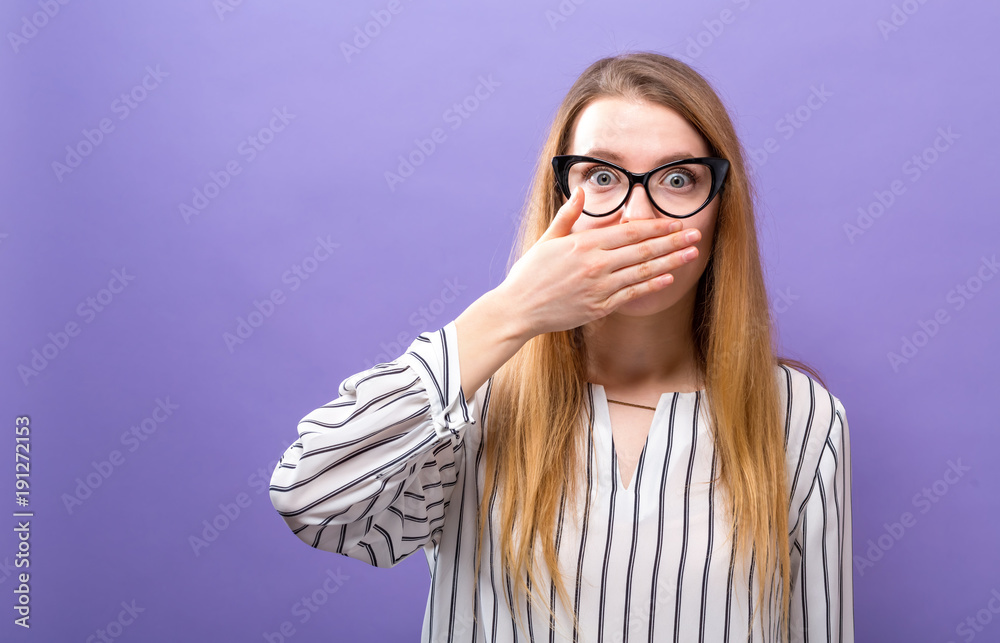Young woman covering her mouth on a solid background