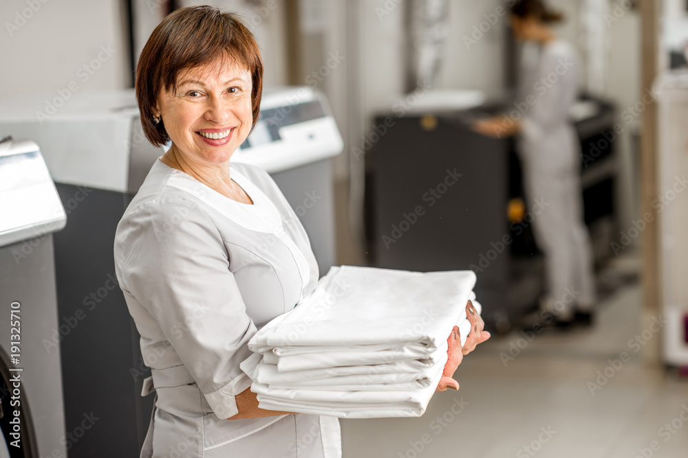 一位穿着制服、拿着床上用品站在酒店洗衣房的资深洗衣女工的肖像