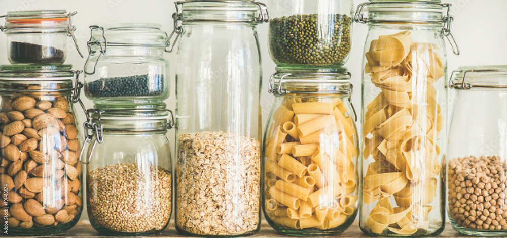在木桌上的玻璃罐中进行健康烹饪的各种未煮熟的谷物、谷物、豆类和意大利面，