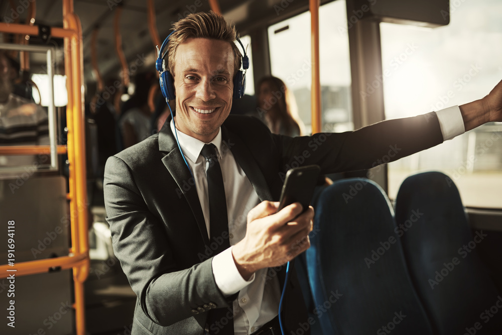 Smiling young businessman standing on a bus listening to music