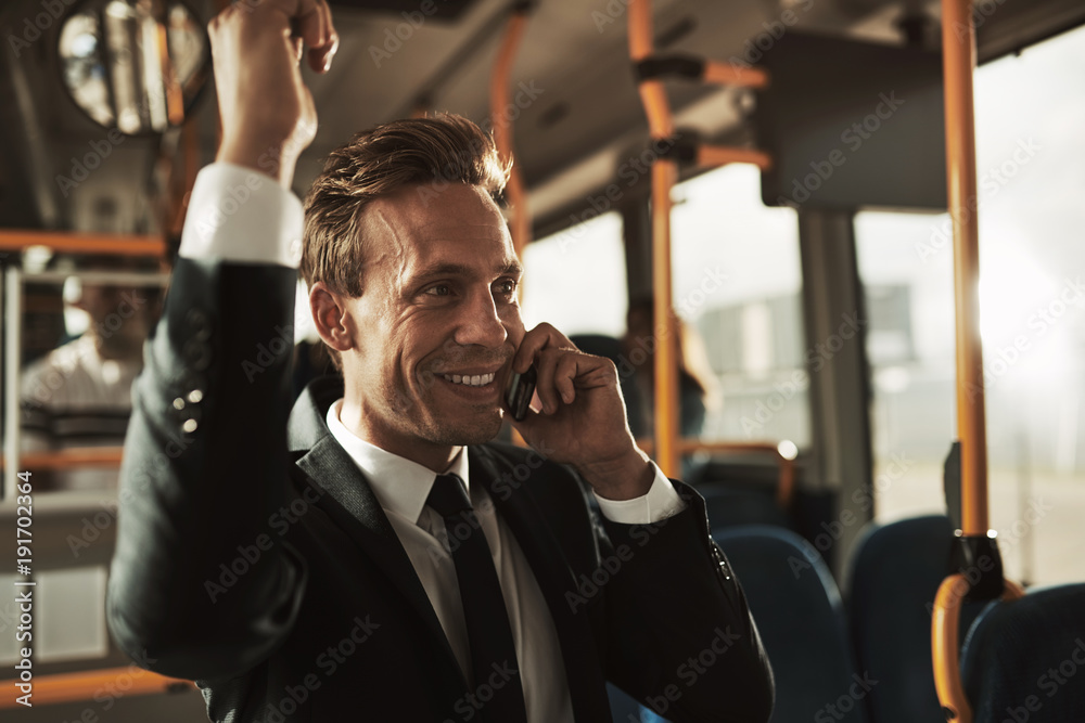 微笑的商人站在公交车上用手机聊天