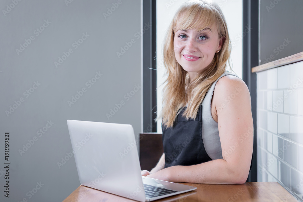 企业主高加索女人拿着菜单，穿着围裙，拿着笔记本电脑，在咖啡店后面工作