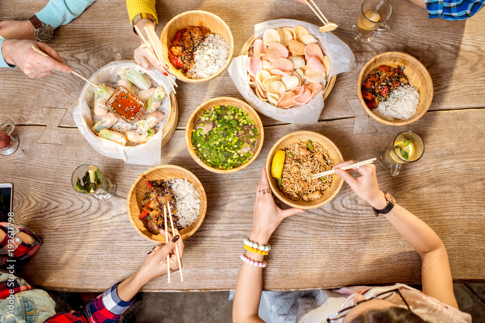 餐桌上的俯视图，桌上摆满了装在木板里的不同亚洲饭菜，年轻人在吃