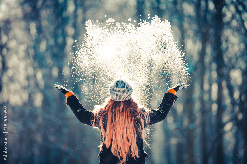 年轻女孩在阳光明媚的冬日向空中扔雪，后视