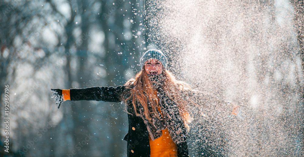 阳光明媚的冬日，微笑的女人向空中扔雪