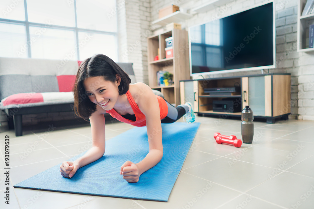 亚洲女人，她在瑜伽垫上假装平板。她在家锻炼。