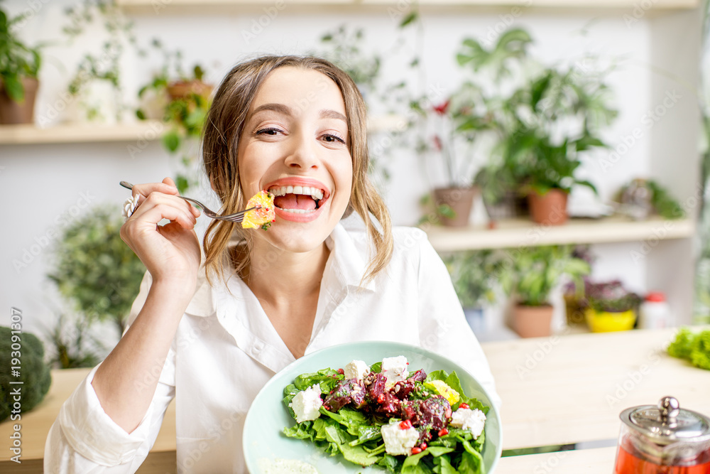 年轻女性坐在美丽的室内吃健康食品，背后开着绿色的花朵