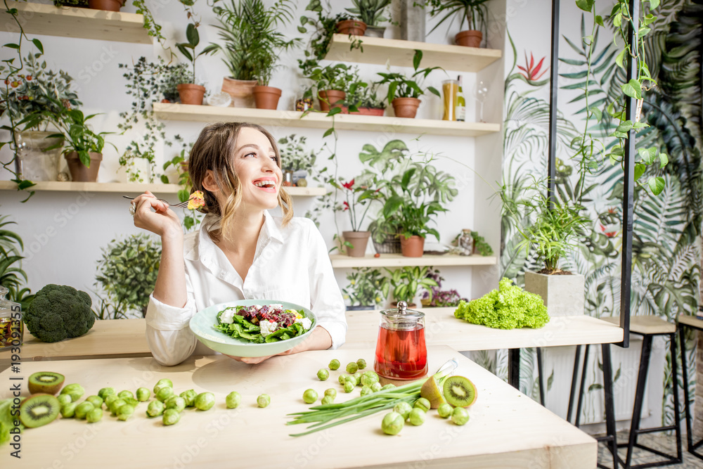 年轻女性坐在美丽的室内吃健康食品，背后开着绿色的花朵