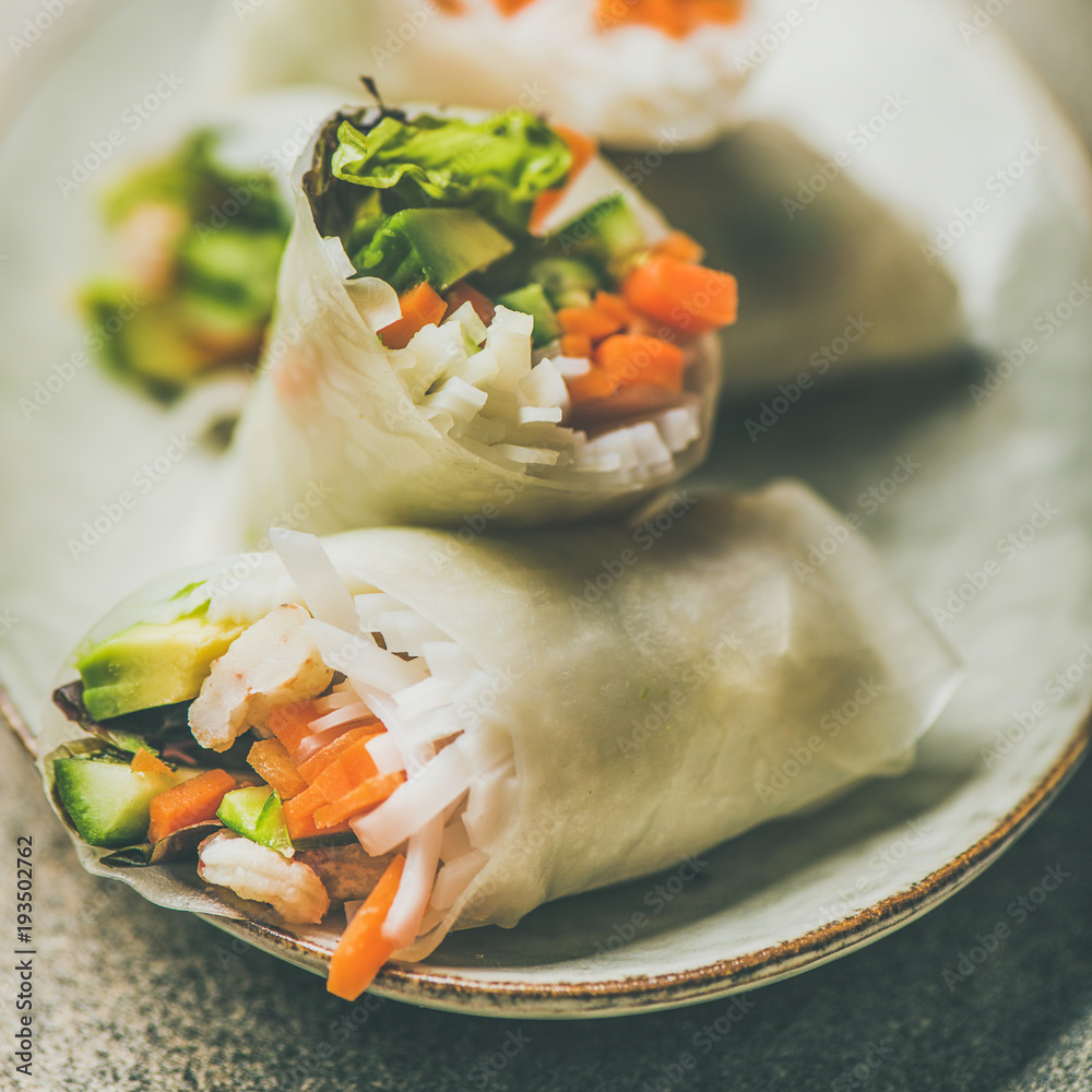Shrimp and vegetable rice paper spring rolls with sauce on plate over grey background, selective foc