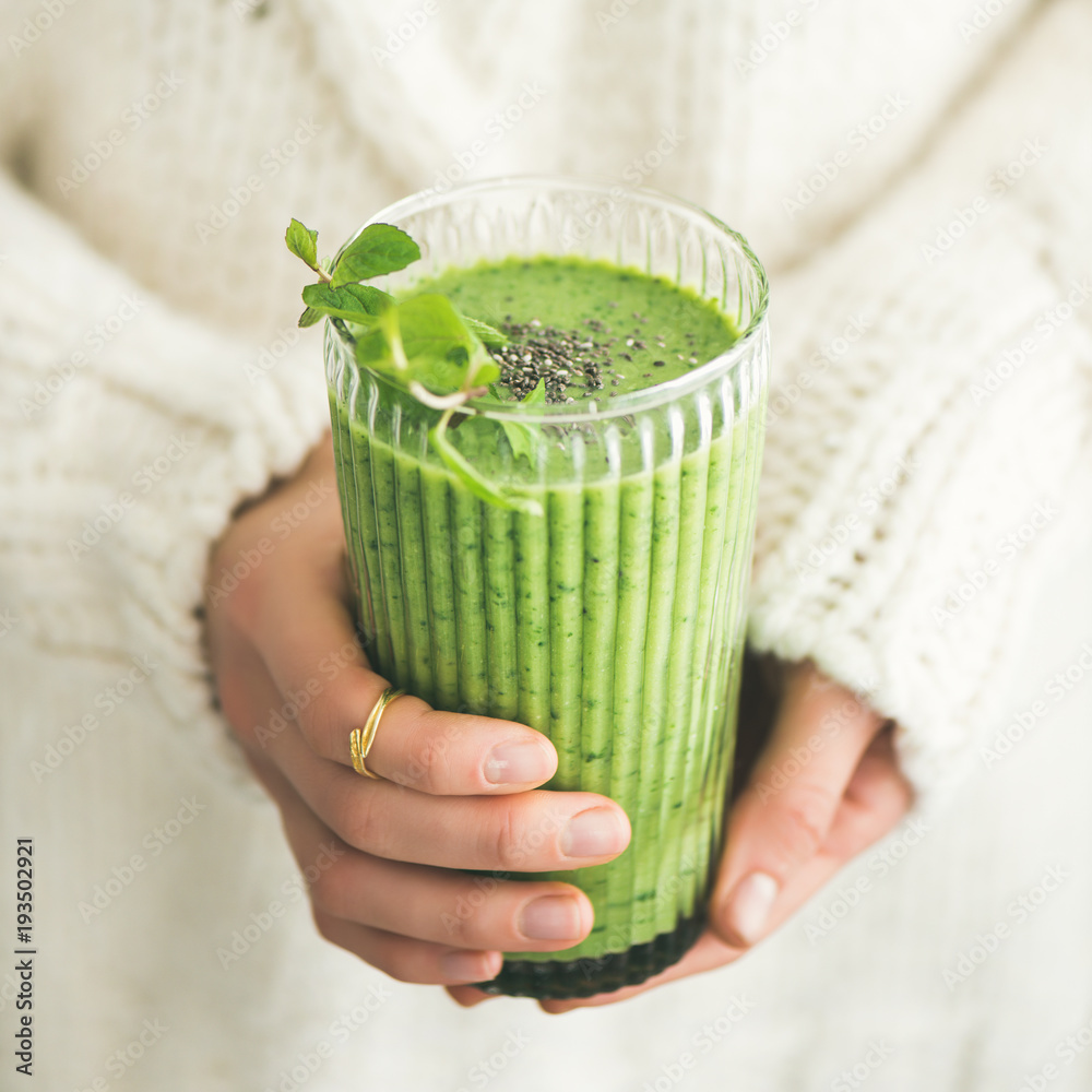 Matcha green vegan smoothie with chia seeds and mint in glass in hands of female wearing white sweat
