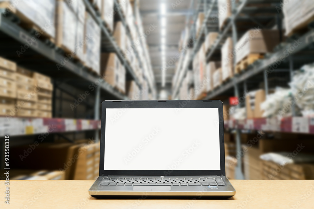 Laptop with white blank screen on brown wooden desk and blurred warehouse store background.