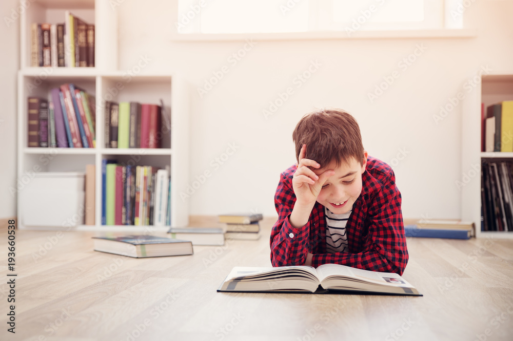 Eight years old child lying on the floor among books at home. Serious boy reading in white room
