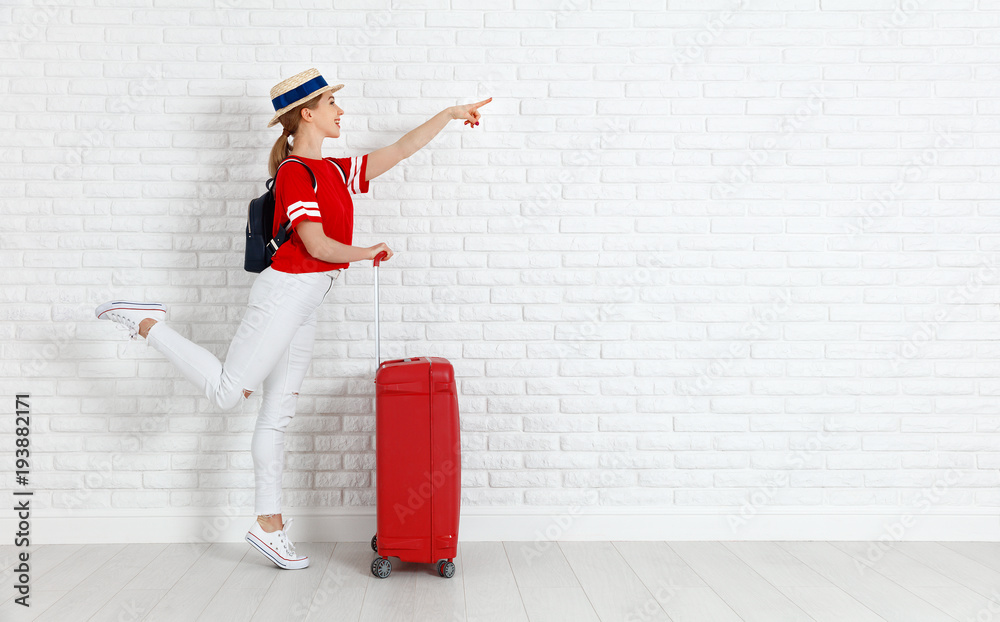 概念旅游。白色空砖墙附近提着红色行李箱的女孩