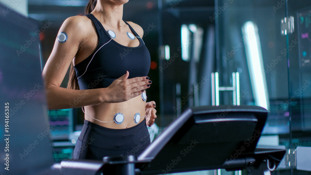 美女运动员身体在跑步机上运行，身体上附着电极，女性生理学