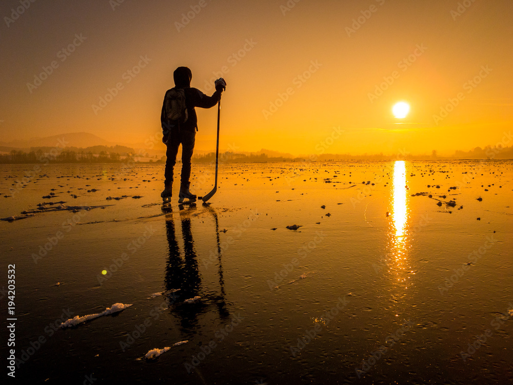 日落时结冰湖面上的冰球运动员