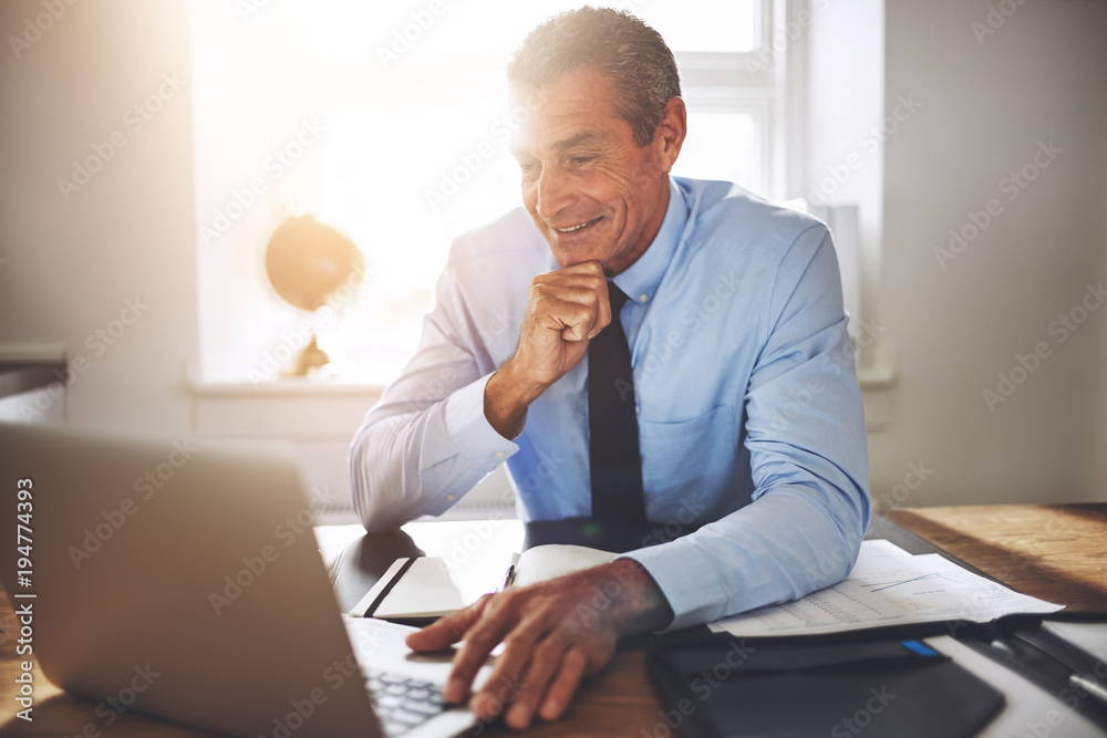 微笑的成熟商人在办公桌上在线工作