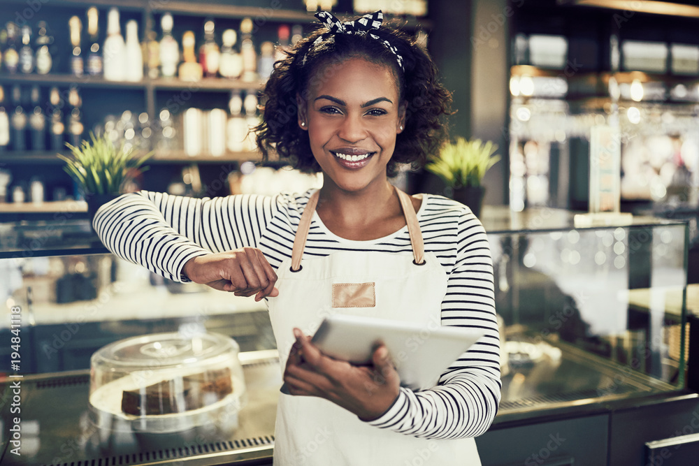 Smiling African entrepreneur standing in her cafe with a tablet