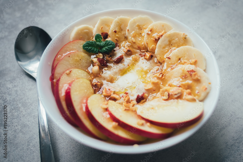 白碗燕麦配香蕉、坚果、苹果和蜂蜜。天然健康减肥食品