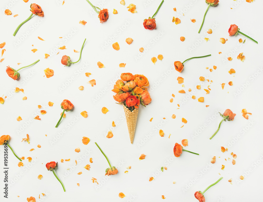 Flat-lay of waffle sweet cone with orange buttercup flowers over white background, top view. Spring 