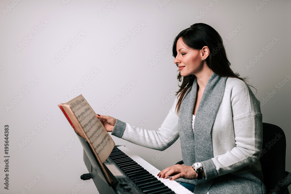 迷人的音乐家在合成器上用乐谱练习古典钢琴演奏。