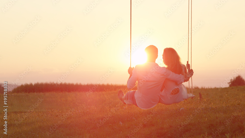 LENS FLARE：在阳光明媚的夏夜，一对幸福的情侣在秋千上摇摆。