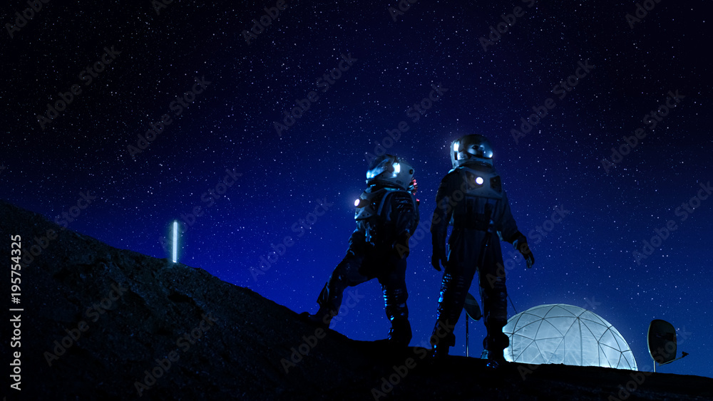 两名身穿太空服的宇航员站在月球上，看着布满星星的美丽夜空。in