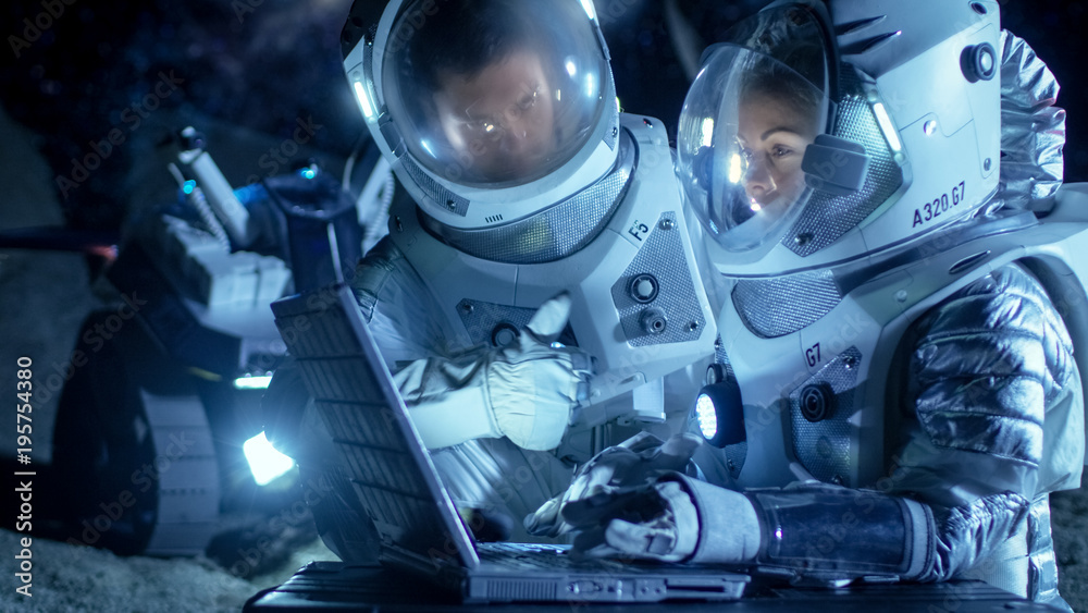 两名宇航员穿着太空服在笔记本电脑上工作，探索新发现的行星，交流