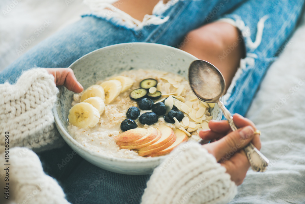 Healthy winter breakfast in bed. Woman in woolen sweater and shabby jeans eating vegan almond milk o