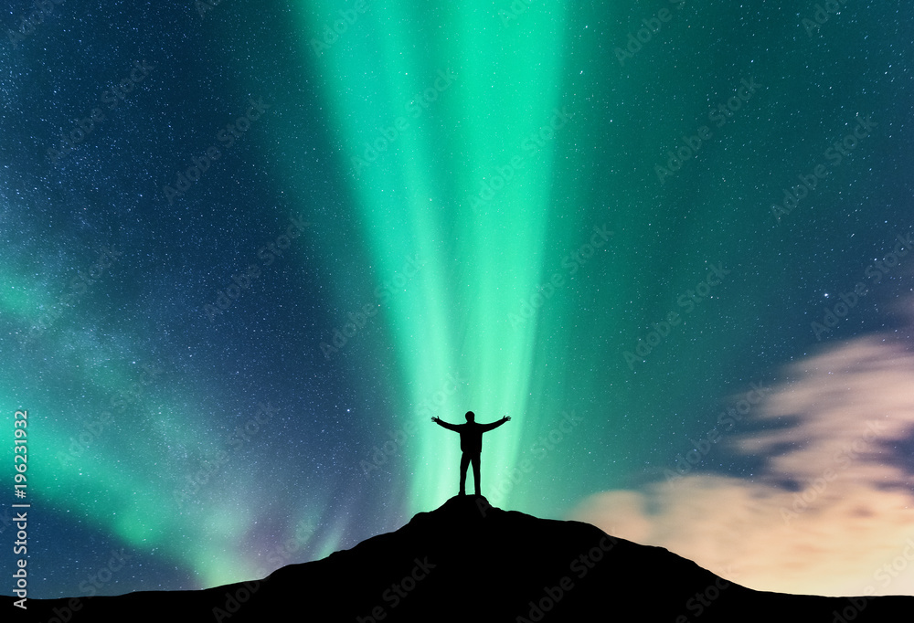 Aurora and silhouette of standing man with raised up arms on the mountain. Lofoten islands, Norway. 