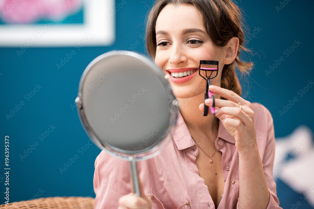 室内蓝色墙壁背景上坐着镜子，用睫毛夹的年轻女子