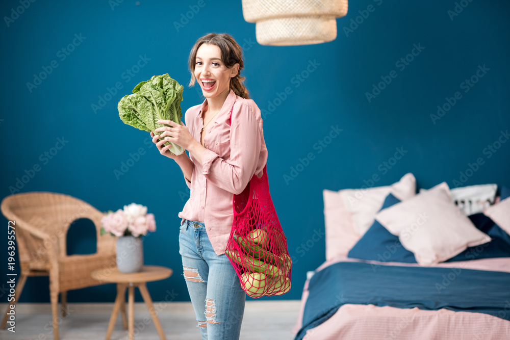 一位年轻女子的画像，她站在一个装满绿色蔬菜的红色袋子里，手里拿着一棵生菜