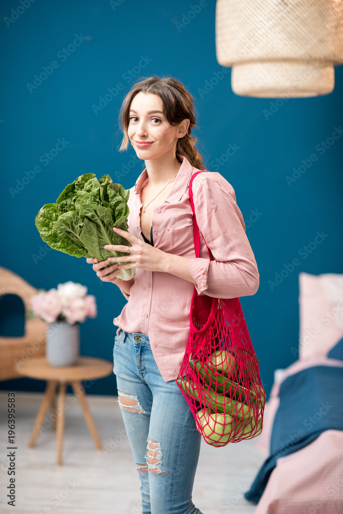 一位年轻女子的肖像，她站在一个装满绿色蔬菜的红色袋子里，手里拿着一棵生菜