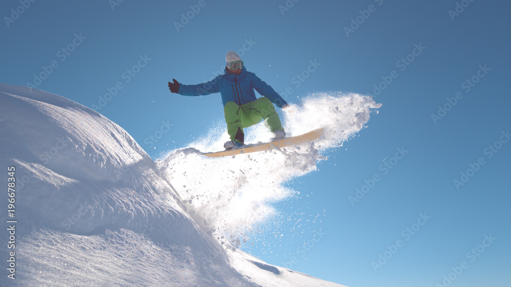 特写：职业单板滑雪运动员在新鲜的雪中跳跃，在阳光下喷洒雪花