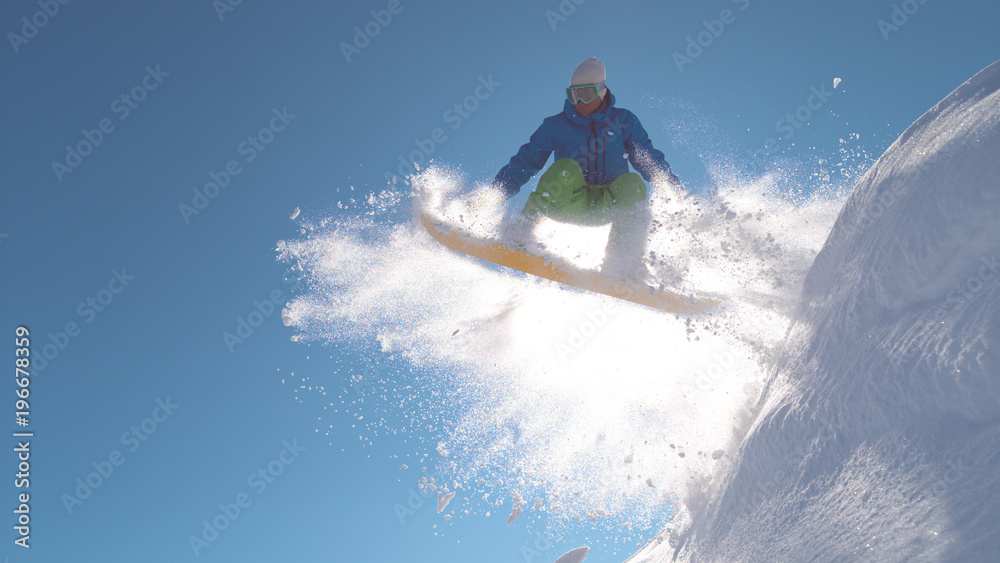 特写：冬日里，在阳光明媚的山区，滑雪板手在粉雪中跳跃。