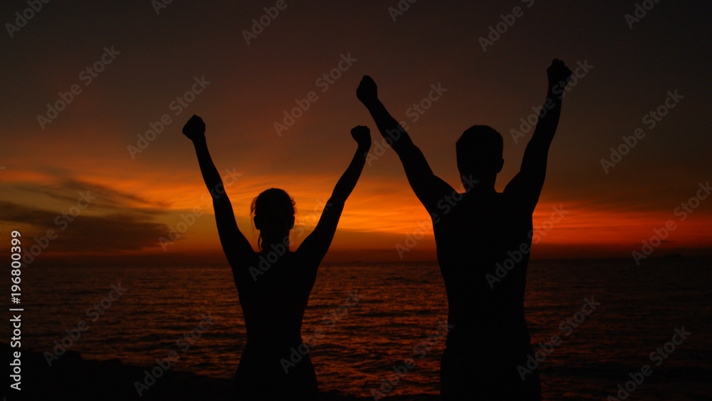 特写，沉默：激动的夫妇在日落时胜利地张开双臂。
