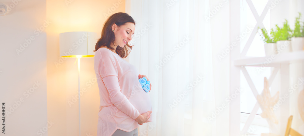 Pregnant woman touching her belly and playing with little baby shoes. Happy pregnant middle aged mot