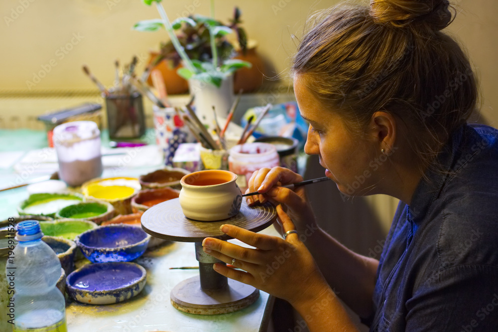 在陶艺工作室工作的女人。陶艺工作室。在陶器中的粘土杯上作画。