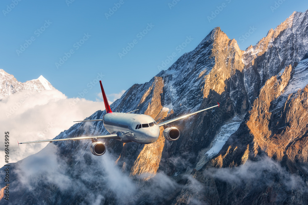 飞机在晴朗的日子里飞越低云，背靠白雪皑皑的山峰。风景。通行证