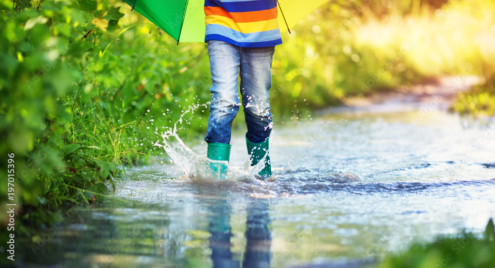 雨天，孩子穿着雨鞋在水坑里行走。苏州，男孩在雨中撑着五颜六色的伞