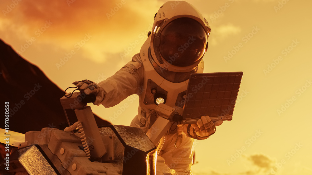 穿着太空服的宇航员在笔记本电脑上工作，在一颗新的外星红色星球上调整漫游者，大概是M