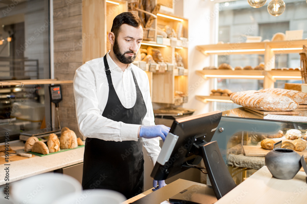 英俊的面包销售商在一家小而舒适的面包店里用收银台工作
