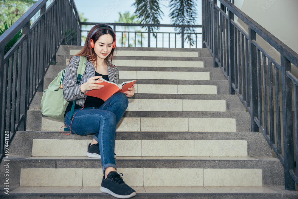 一个十几岁的大学生在暑假里微笑着看书。她在听