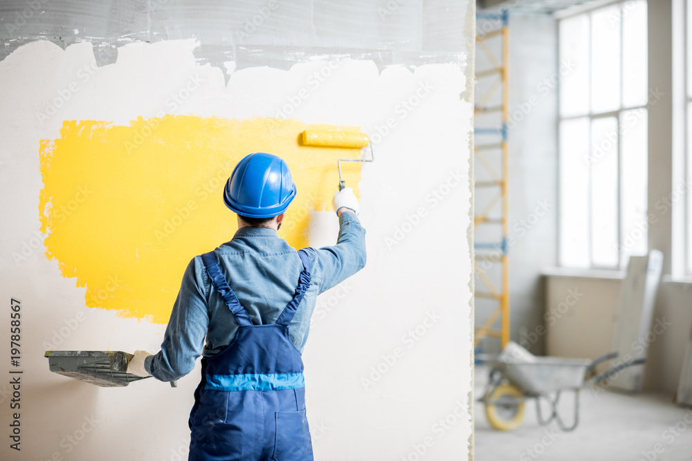 在室内施工现场，工人在统一的墙壁上涂上黄色油漆