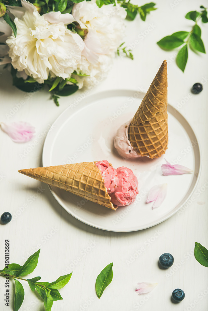 粉红色草莓和椰子冰淇淋勺、甜甜筒和牡丹花在盘子里。