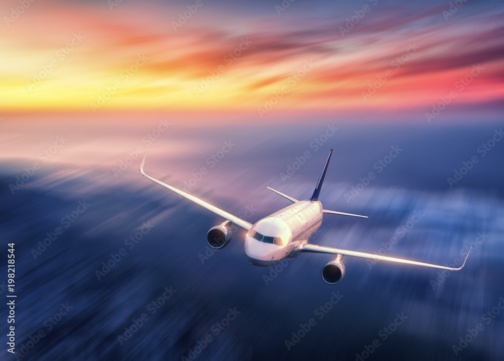 Modern airplane with motion blur effect is flying over low clouds at sunset. Passenger airplane, blu