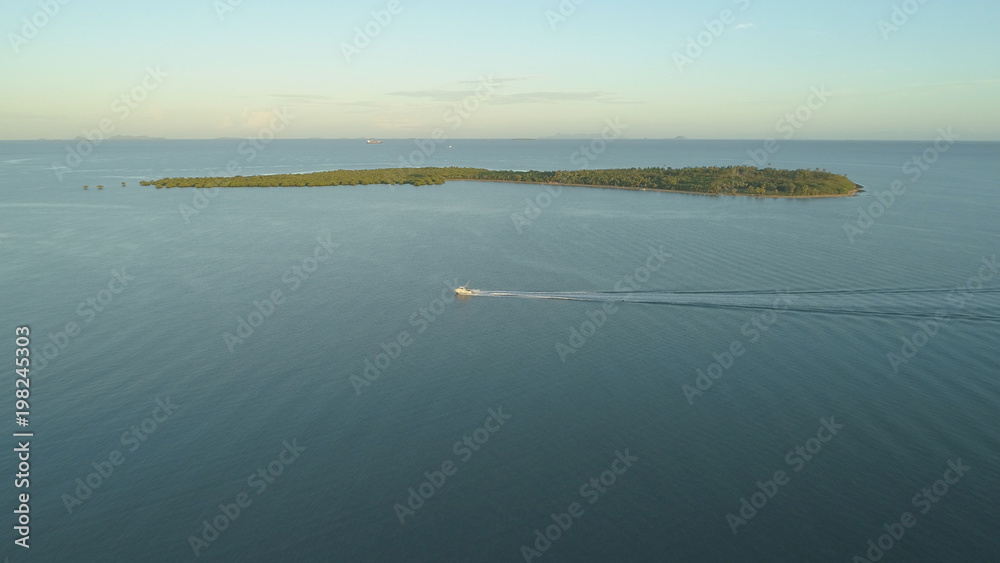 空中航行：一艘小渔船在经过小岛时在蓝色海水中留下一条痕迹