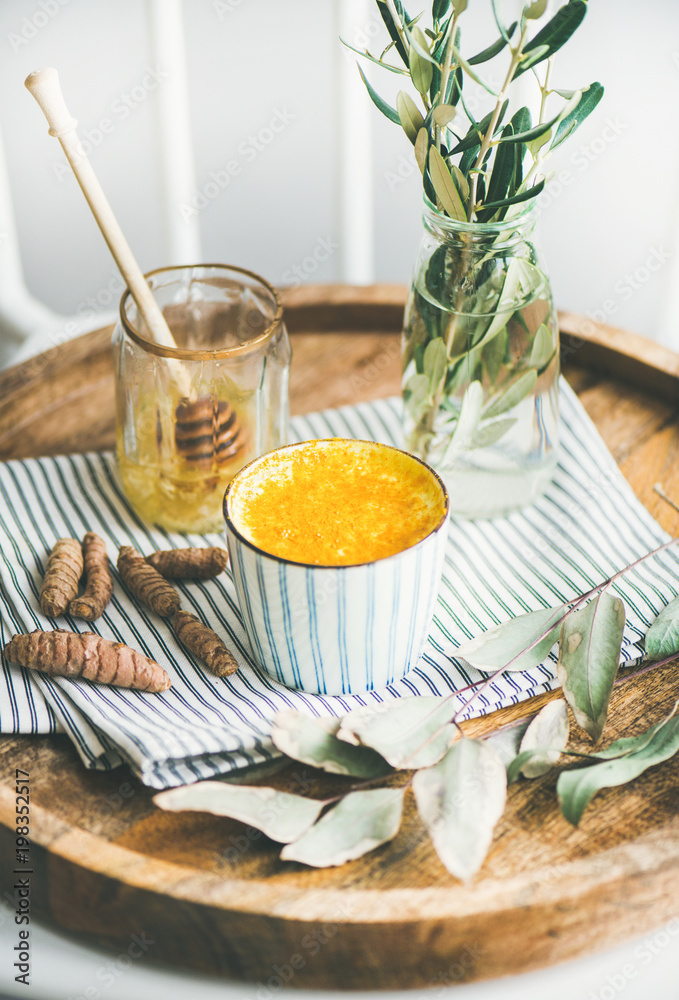 健康纯素食姜黄拿铁或蜂蜜金牛奶，装在木制托盘上的条纹杯中，选择性focu