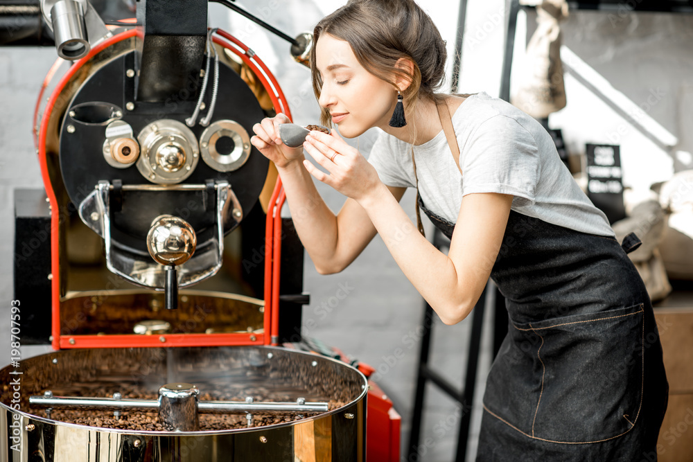 一位女士拿着勺子站在咖啡机旁检查咖啡豆的质量